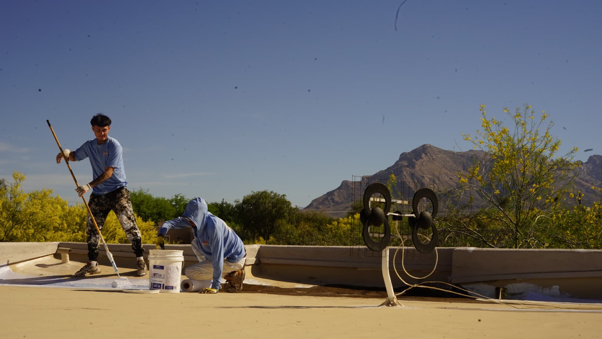Two-person DSR Roofing crew applying fresh roof coating on a Tucson flat roof